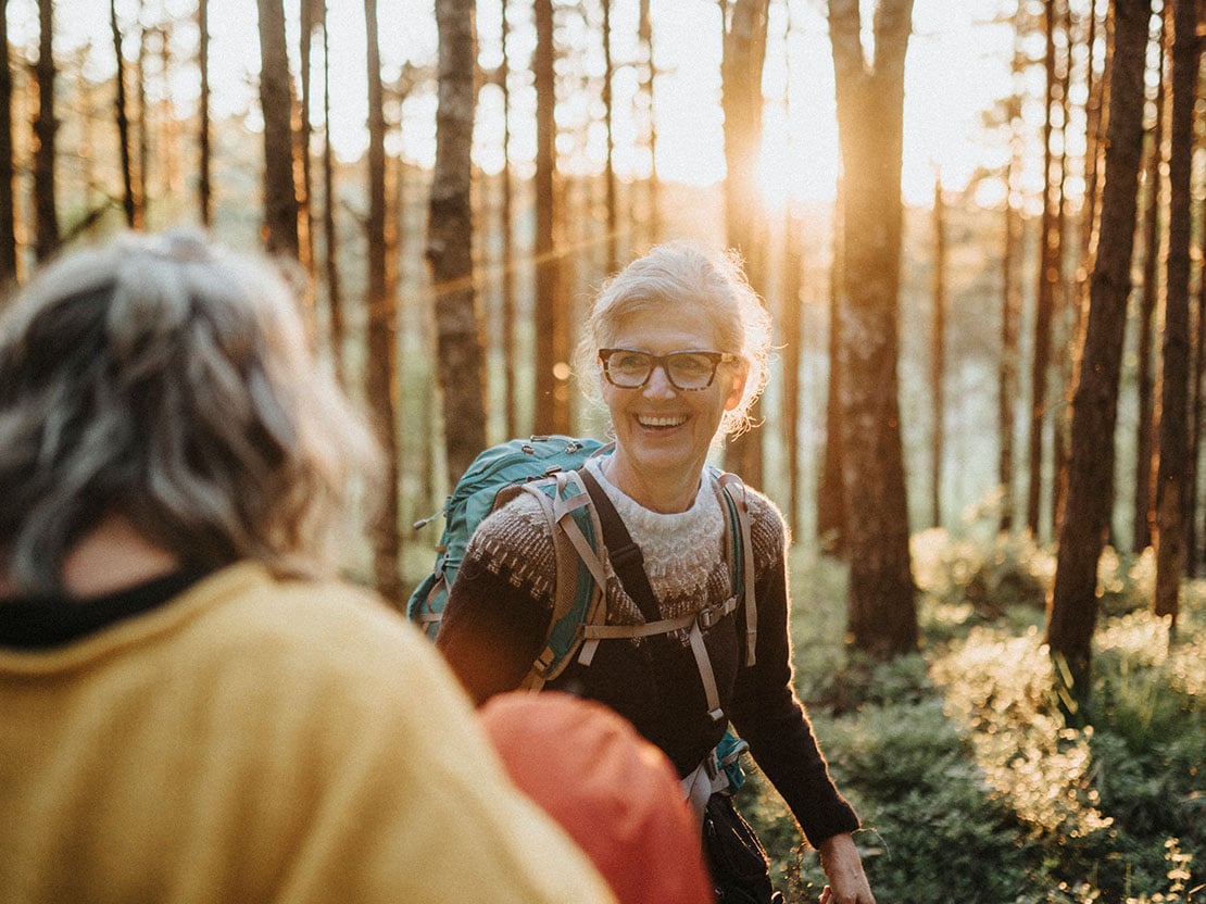 Två friluftsklädda kvinnor i skogen i motljus