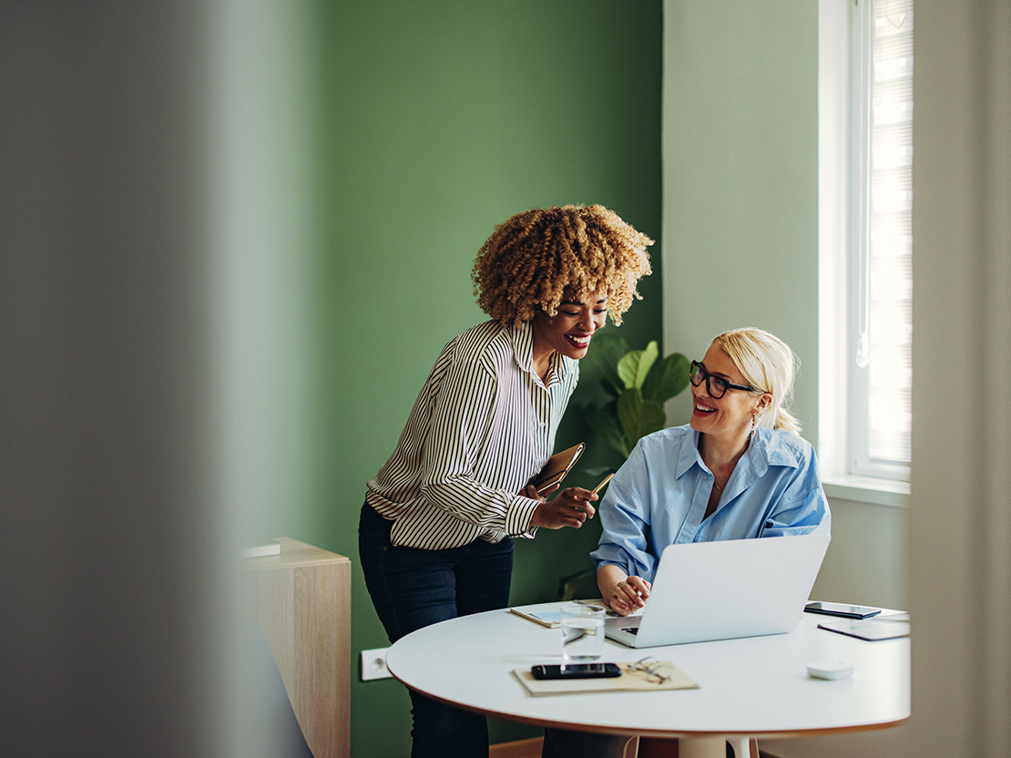 Två leendes kvinnor tittar på laptop i grönt rum